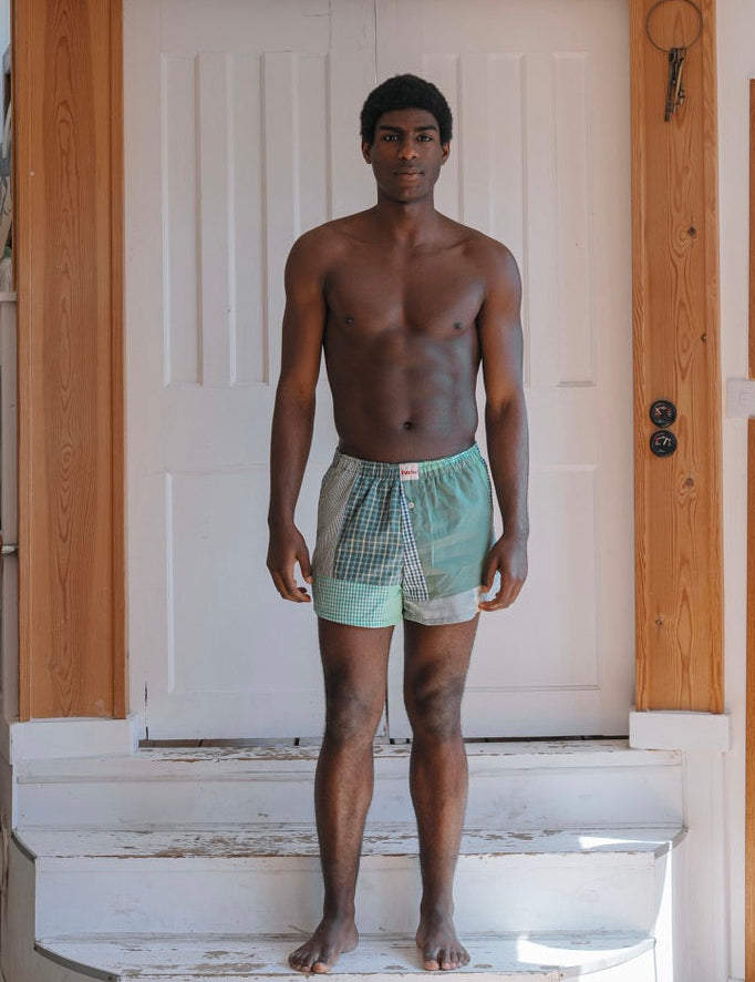 Man standing on a staircase wearing green boxer briefs in a home setting.