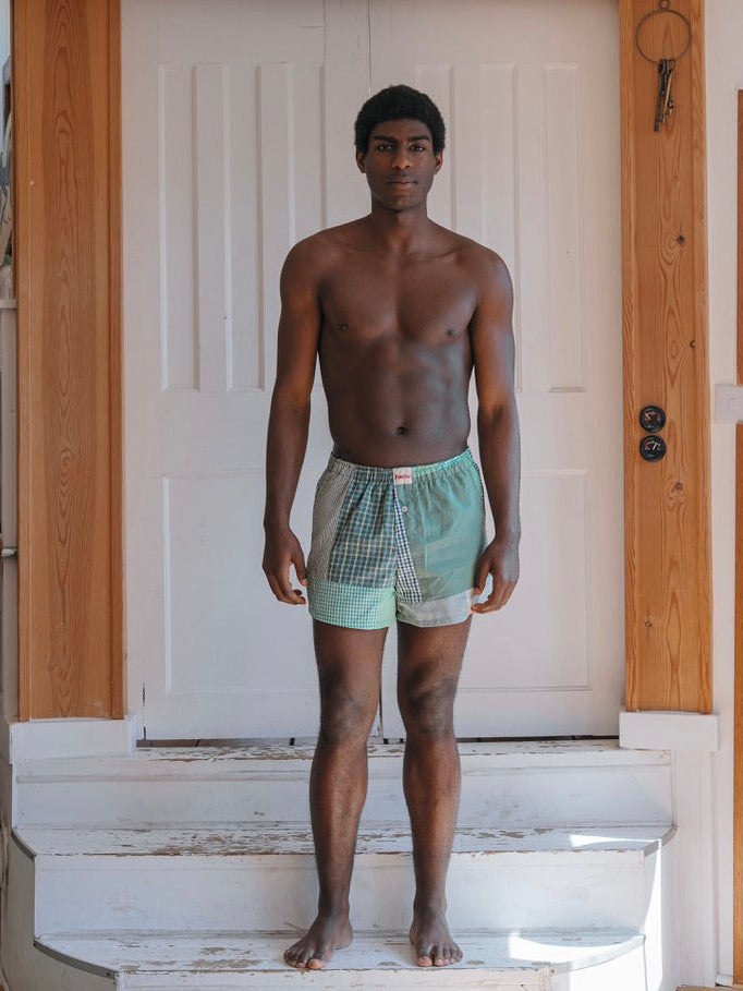 Man standing on a staircase wearing green boxer briefs in a home setting.