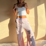 A person wearing baby pink trousers with a wide leg and a white top, standing in a room with sunlight casting a shadow on the wall.
