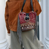 Person wearing a brown jacket and holding a red leather bag with fringe and studs in front of a door.