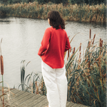 Person standing on a wooden dock by a lake with reeds and trees in the background