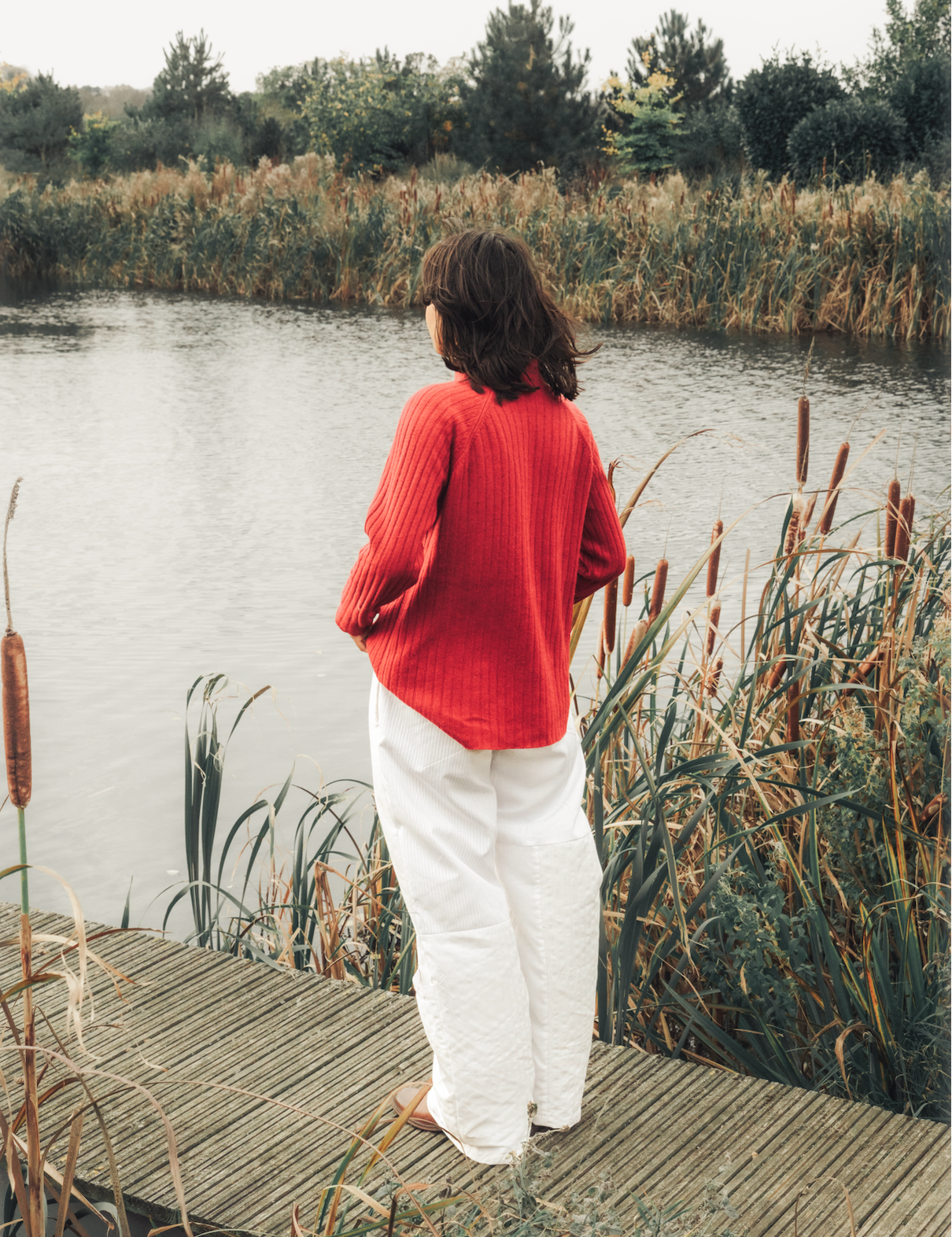 Person standing on a wooden dock by a lake with reeds and trees in the background