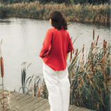 Person standing on a wooden dock by a lake with reeds and trees in the background
